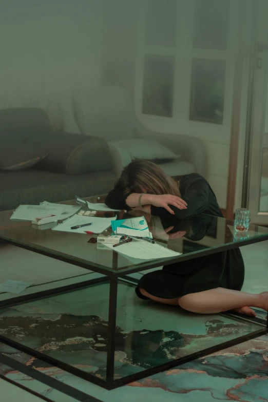 woman sitting under a coffee table rubbing her head