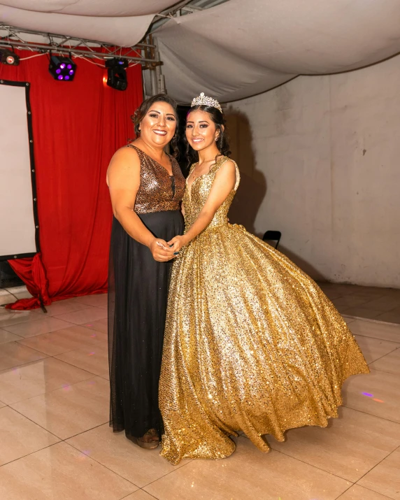 two woman dressed in long gold dresses pose for a picture