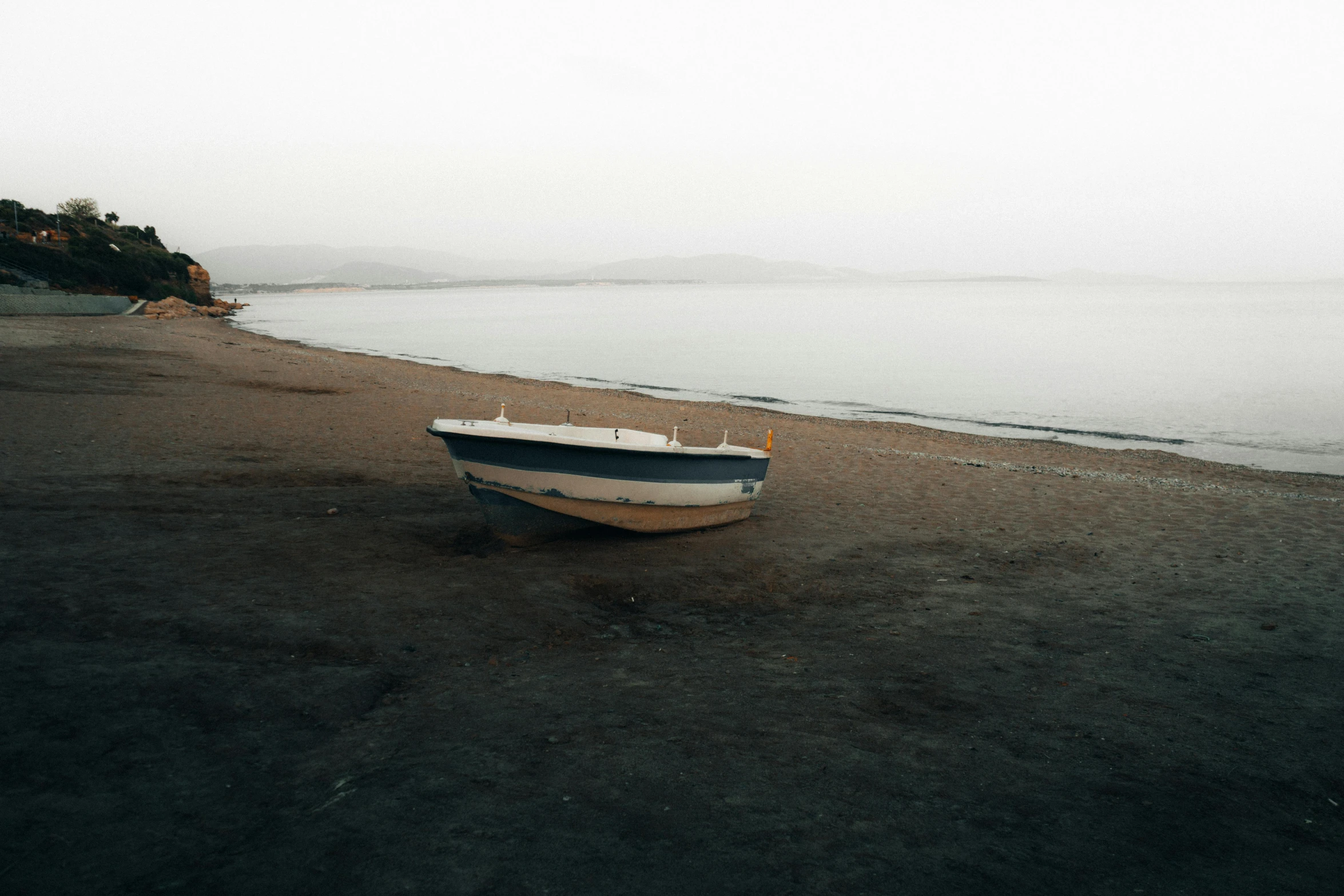 small boat sitting on the sand at the edge of the water