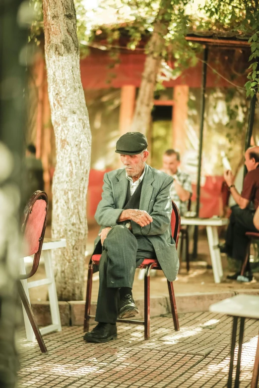 older gentleman sitting on a chair in front of a tree