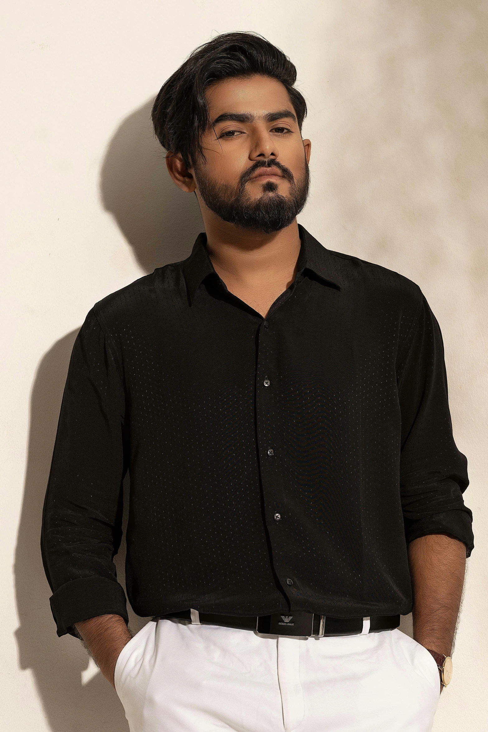 a man in a black shirt and white pants leaning up against a wall