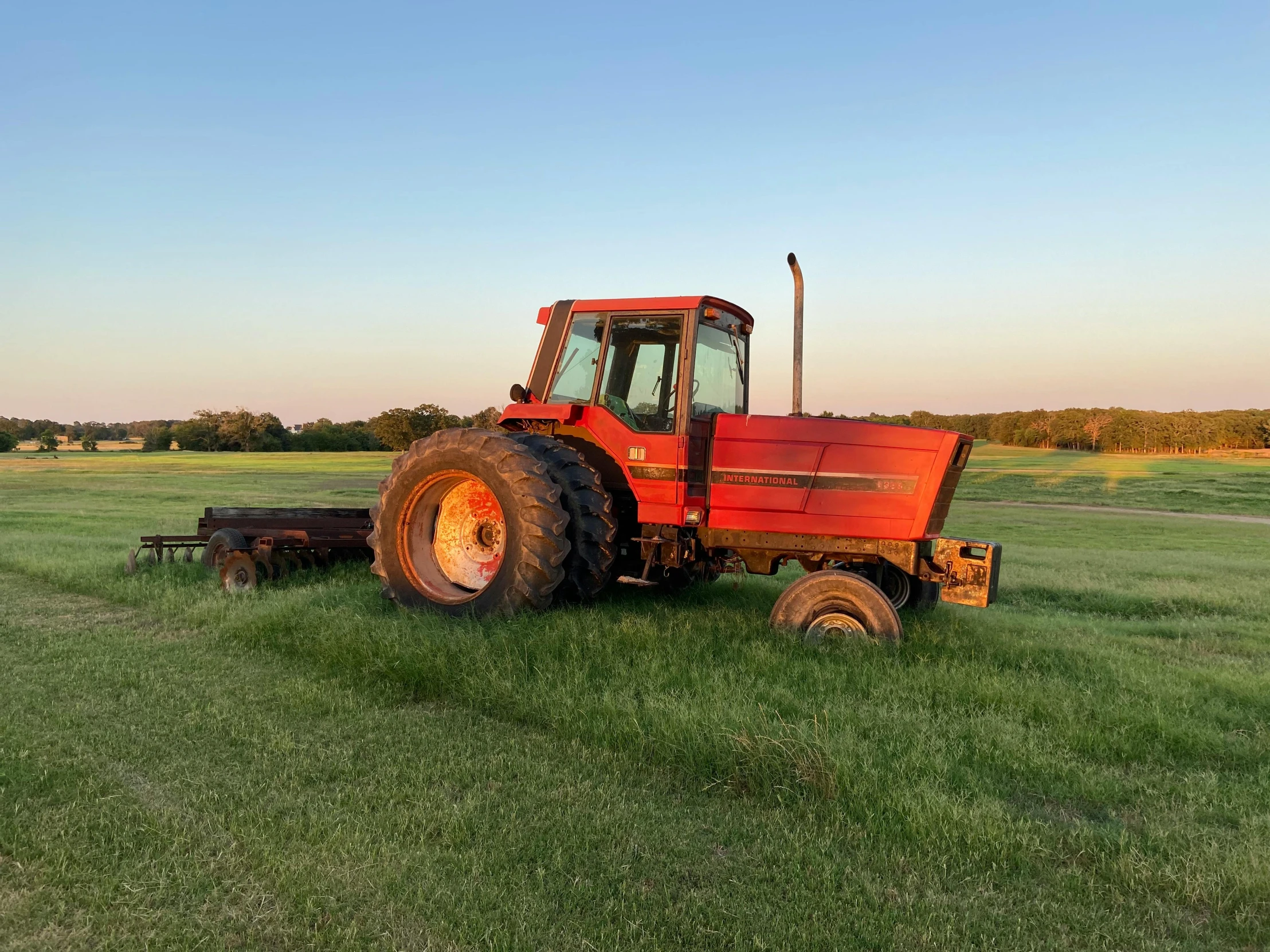 a farm tractor sits in the middle of an empty field