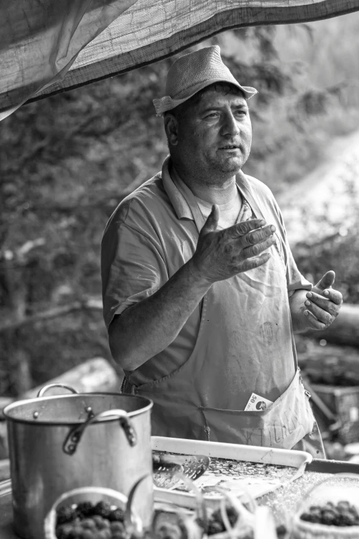 black and white po of man in hat cooking food on a grill