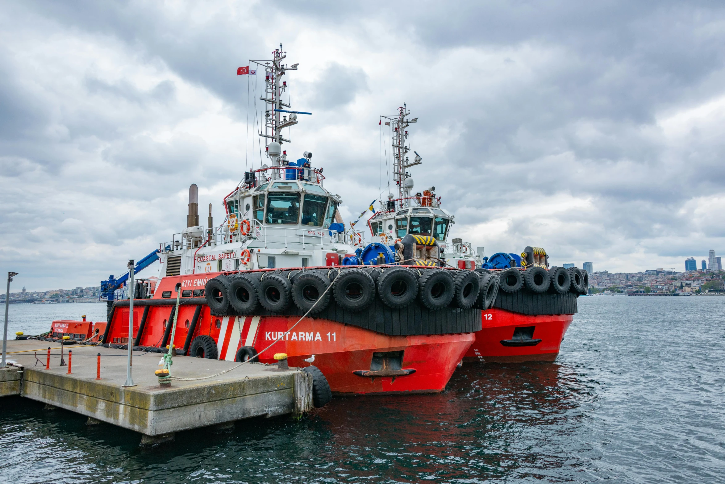 a red tugboat docked at a dock on a cloudy day