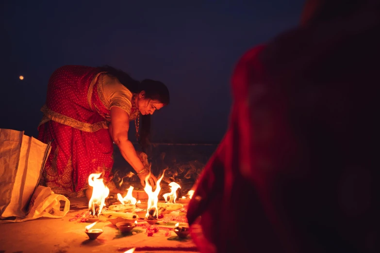 woman kneeling over lit candles while standing next to another