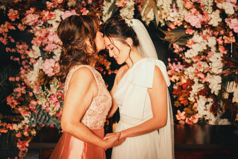 two women in formal dress in front of a flowered wall