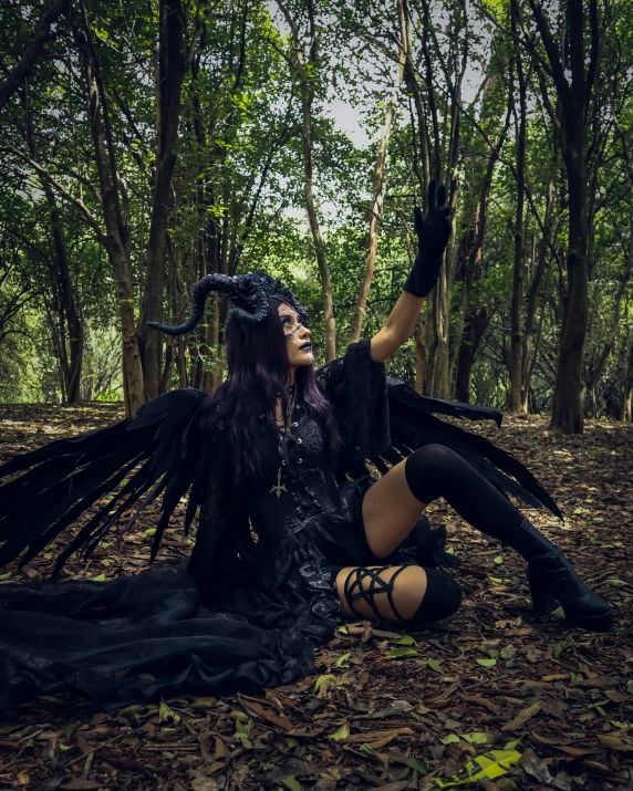 a woman sitting on the ground in a black dress with wings