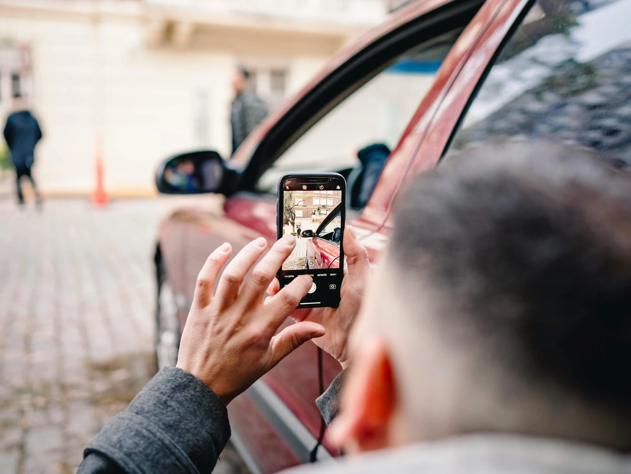 man taking picture on cell phone with reflection on car