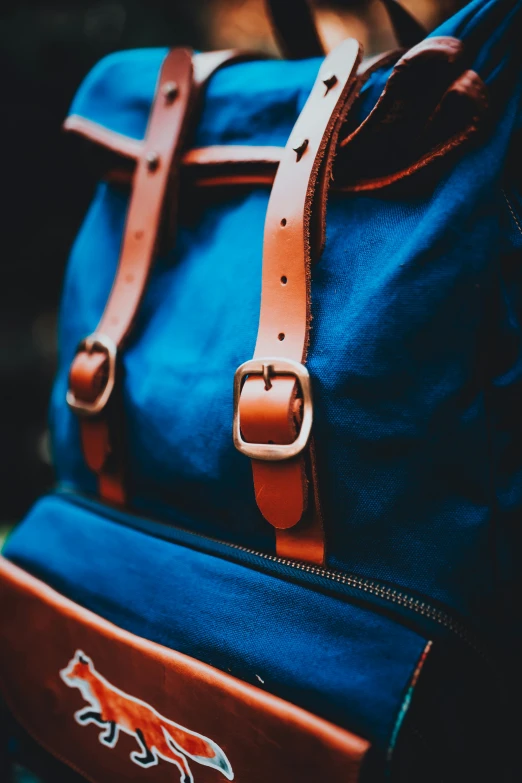 a blue backpack with brown leather straps on top of it