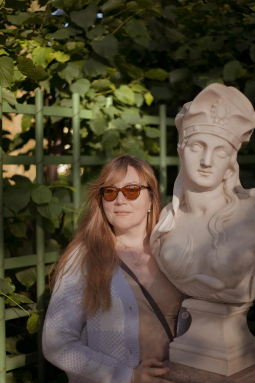 a woman poses next to a statue in the shade