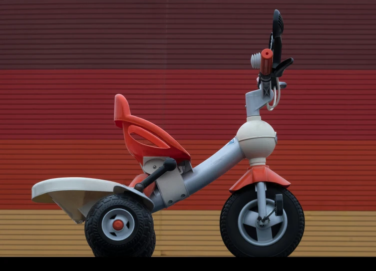 an orange and white tricycle parked in front of a wall