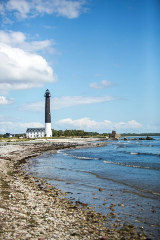 a lighthouse stands on the beach with rocky sand