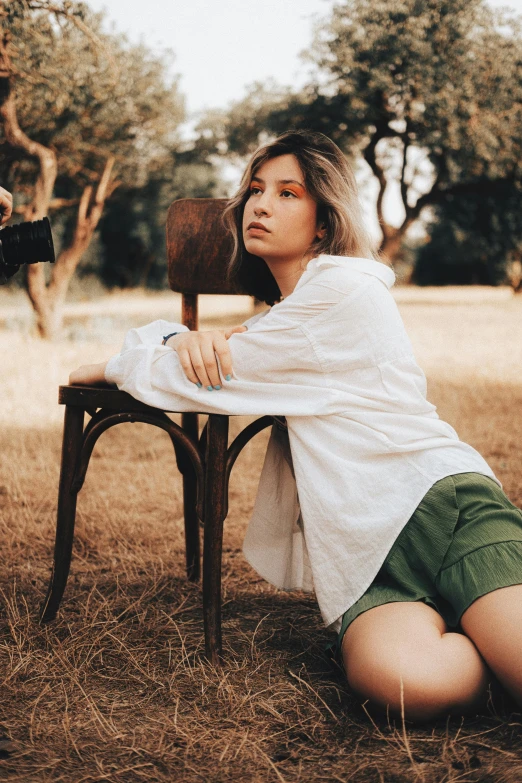 a woman sitting on a wooden chair in front of trees