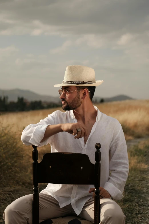 a man in hat, white shirt and pants is leaning against an old fashioned chair