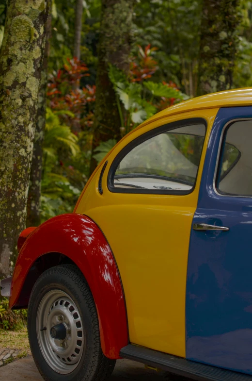 an old yellow and blue car sitting by a tree