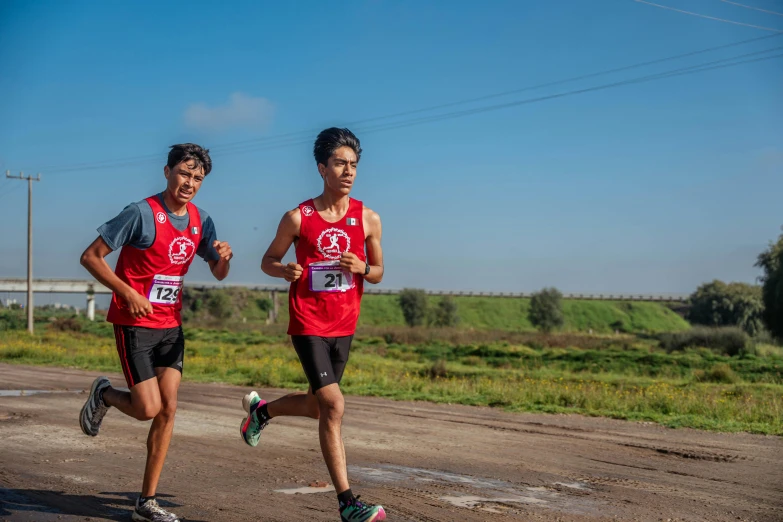 two men running on a dirt road in the middle of the day