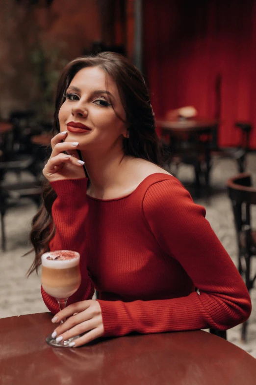 a woman sits at a table with her hand to her face and drinking coffee