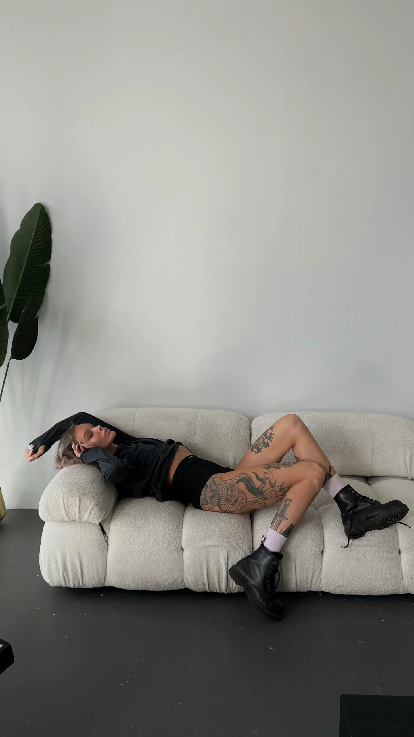 a tattooed woman laying on the back of a white couch