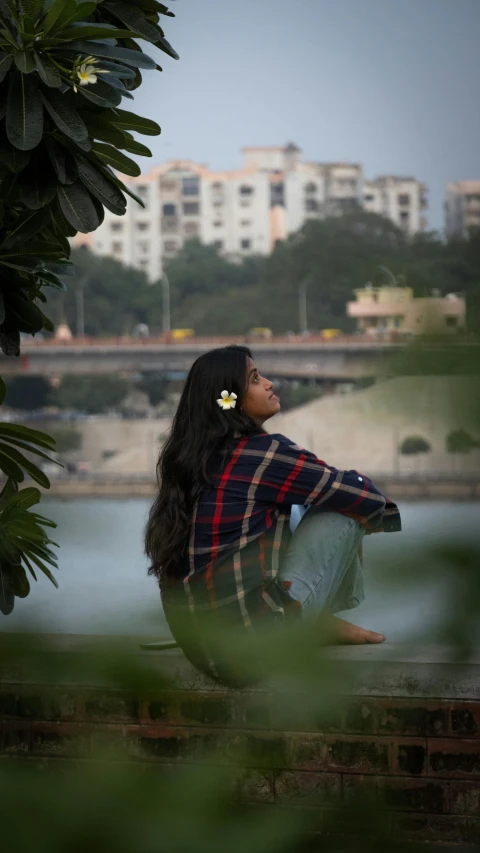 a woman in a plaid shirt is sitting by the river