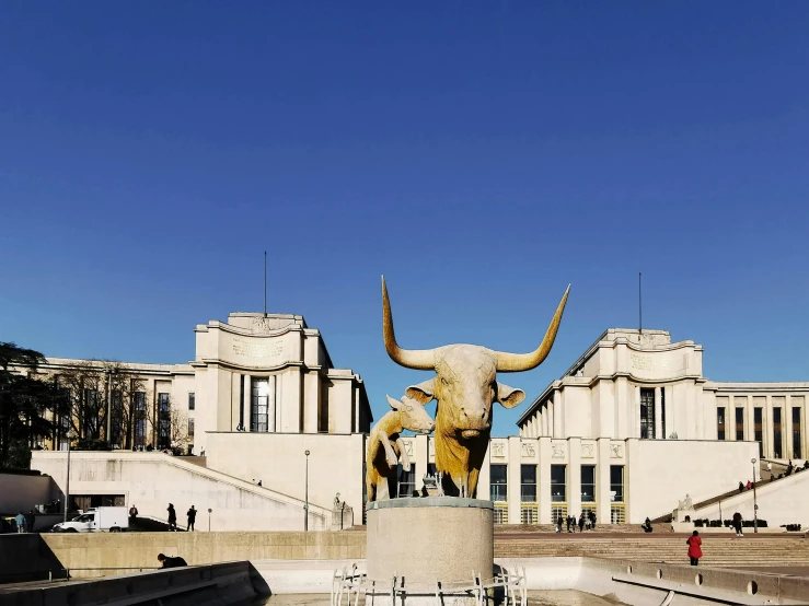 a statue of a cow with horns and large buildings in the background