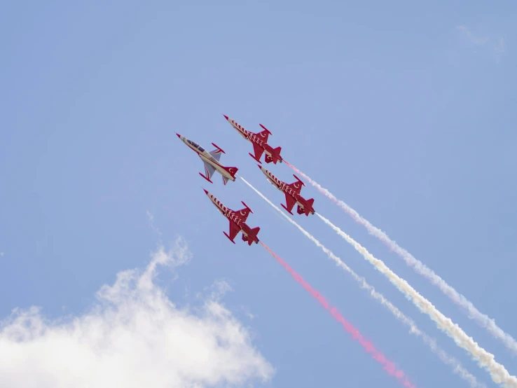 four jets flying in formation with red smoke behind them