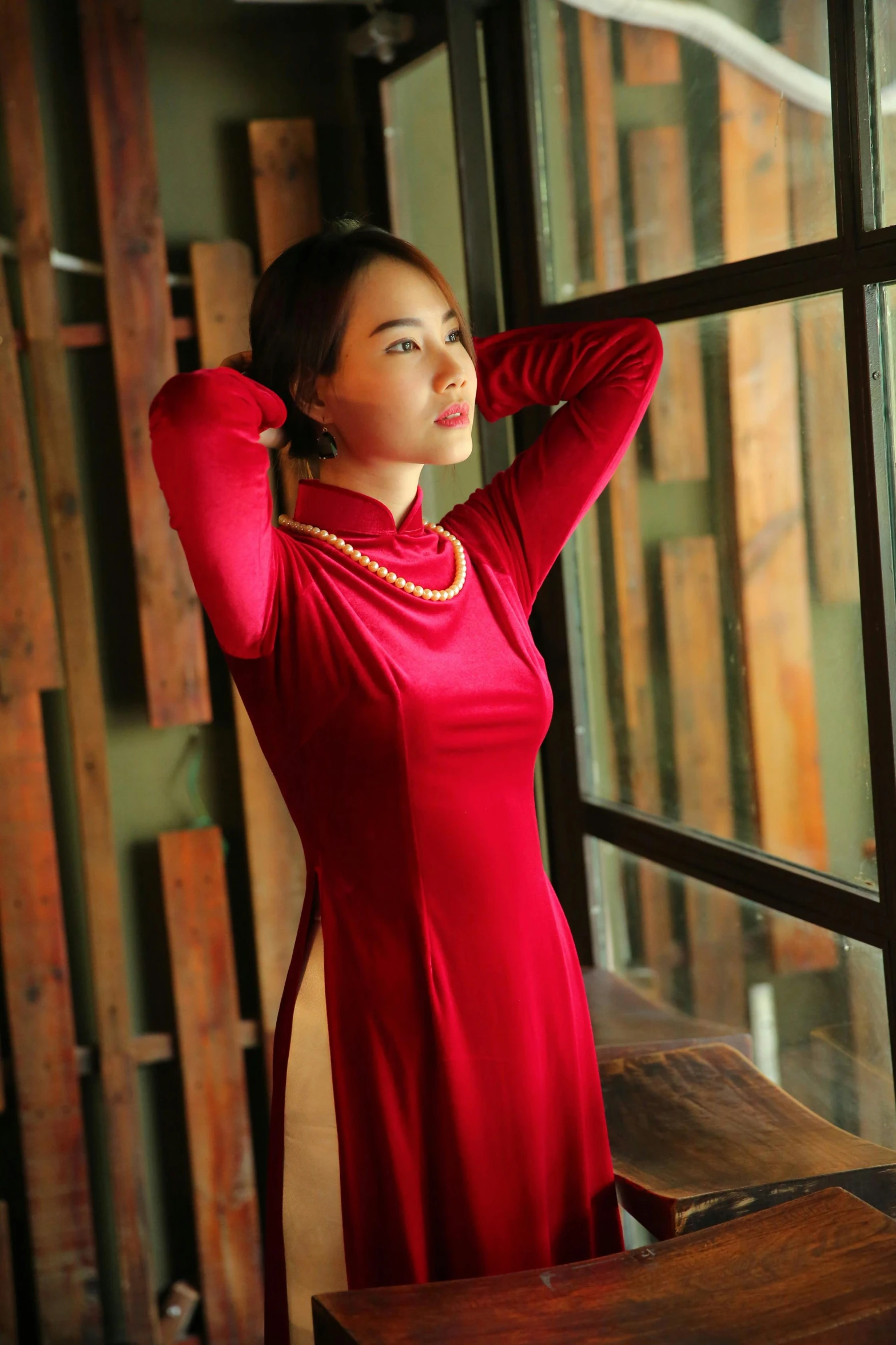 a young woman wearing a red top standing by a window