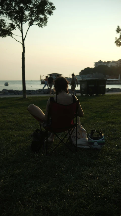 a person sitting on a chair with a backpack in the grass at dusk