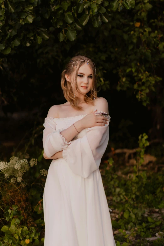 a woman in a white dress standing outdoors with her arms folded over her body