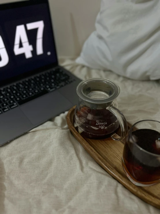 a laptop is on a bed, with some drinks on a tray