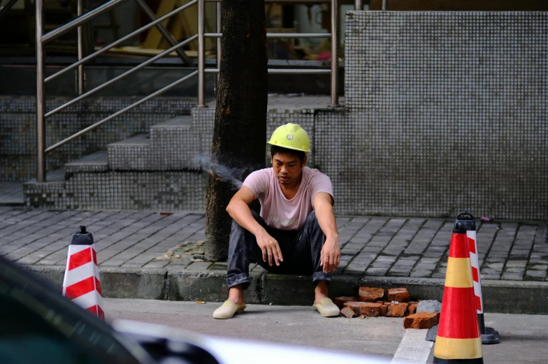 an asian man sitting in the street beside a broken fire hydrant