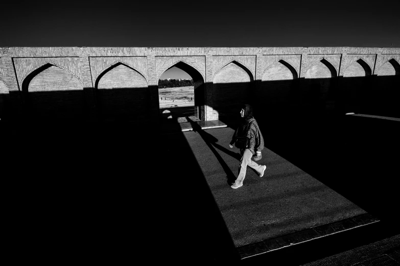 the woman is walking near a bridge in black and white