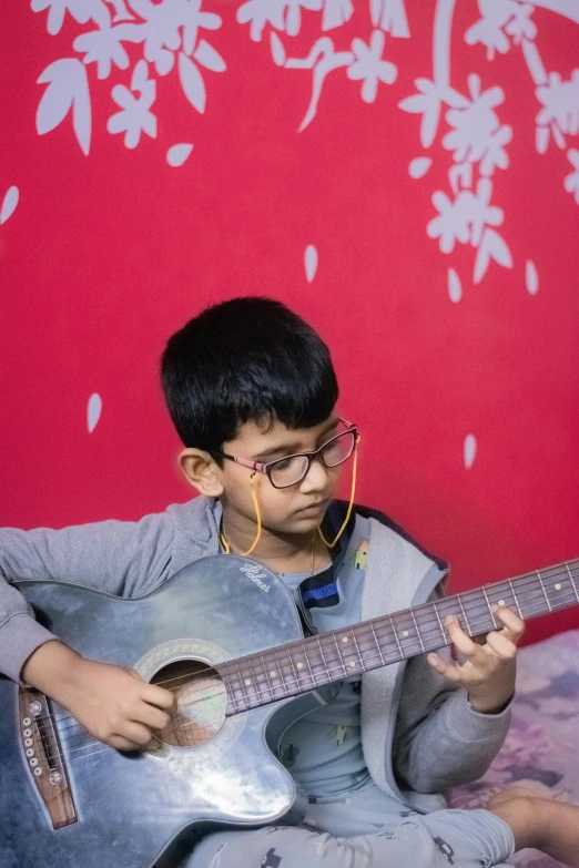 a child sitting down playing a guitar in front of a wall