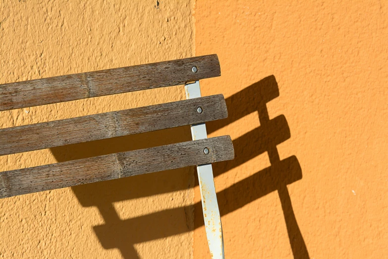 the shadow of a bench casts a cross - country line on an orange wall