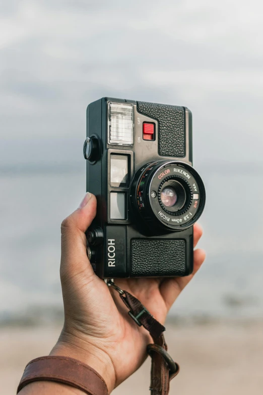 a hand holding an old camera in front of a body of water