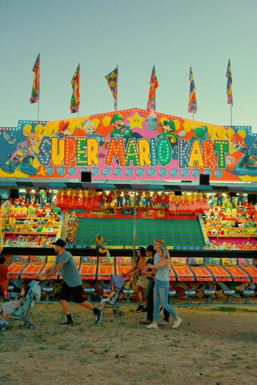 people gather around a carnival attraction, with flags on top