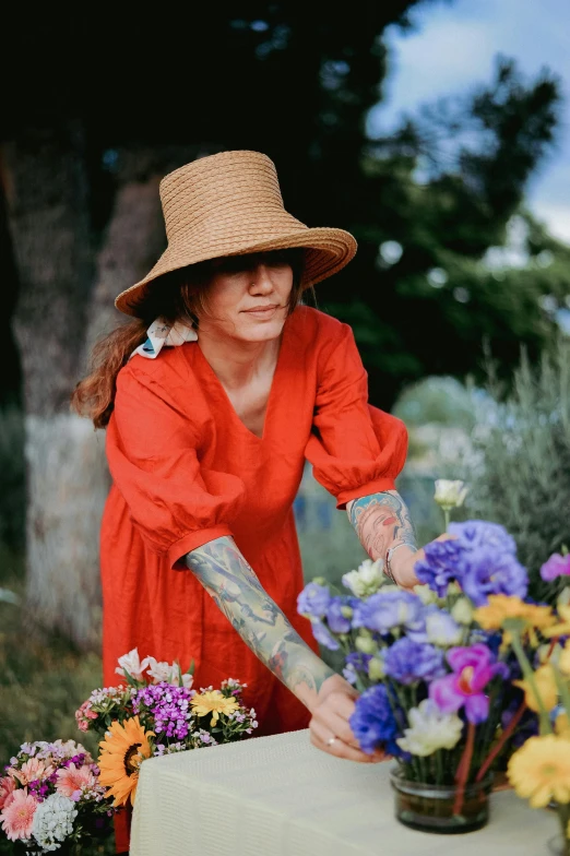 a woman in red dress and large hat placing flowers on a table