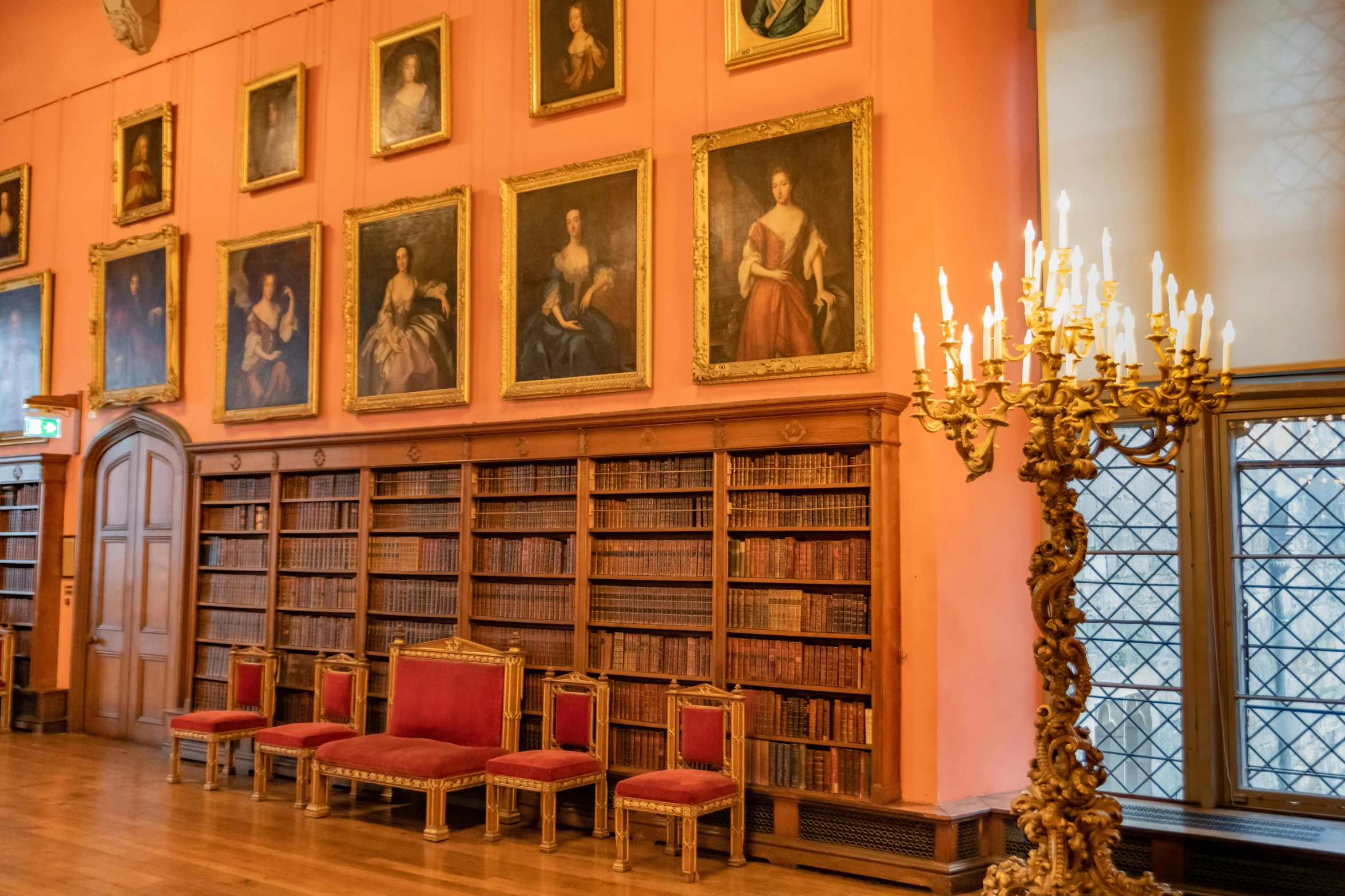 several empty chairs and a candle sit in an old liry with many portraits