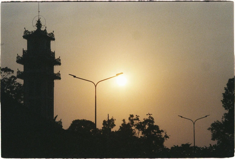 a tower with two lamps near by and the sun in the distance