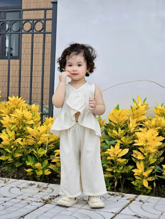 a young child is standing by flowers and pointing her finger up