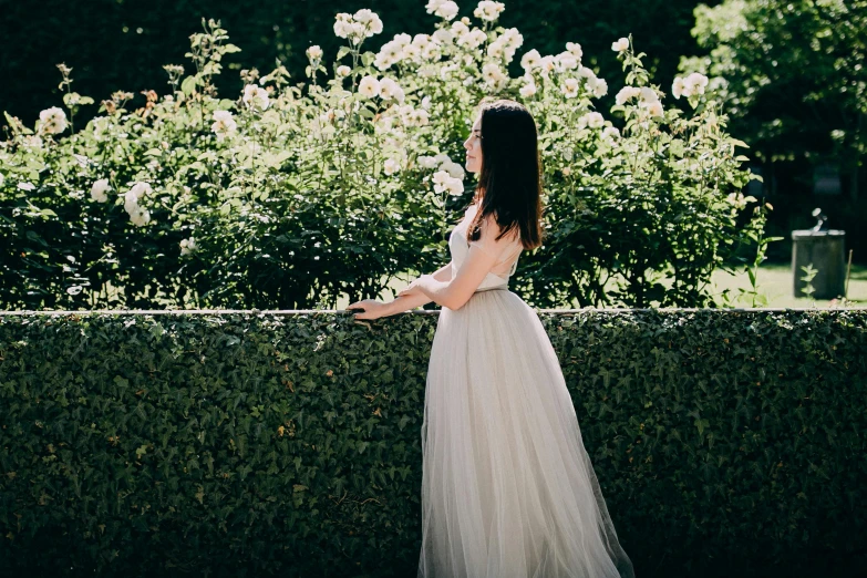 a girl in a gown standing near bushes