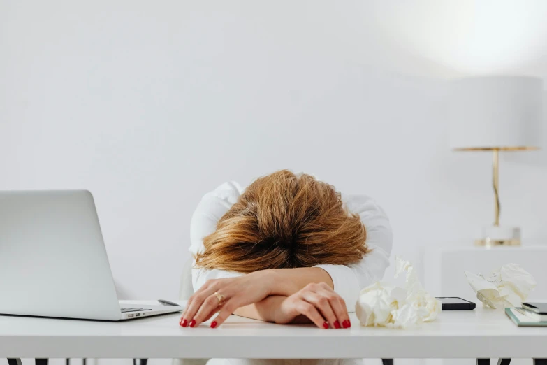 a woman sitting at a table with her head on her desk