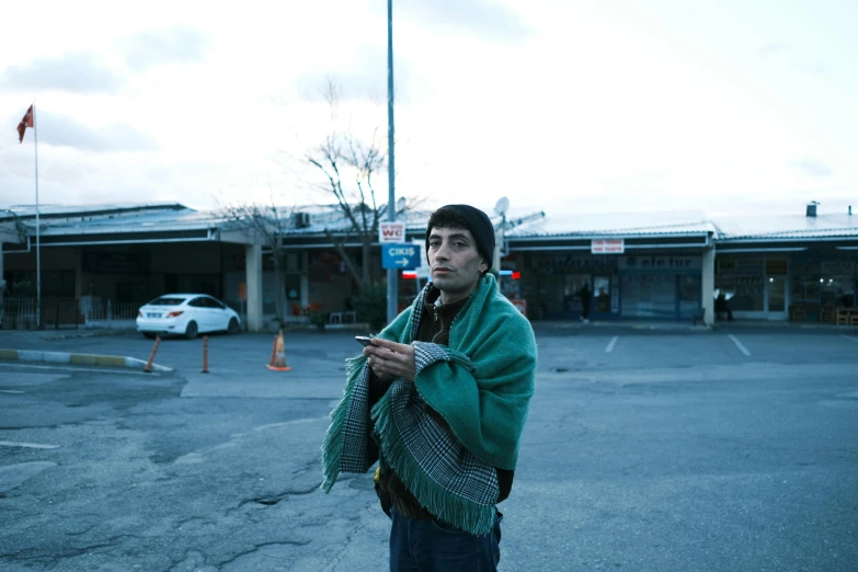 the young man is standing in the parking lot with his coat dd around his shoulders