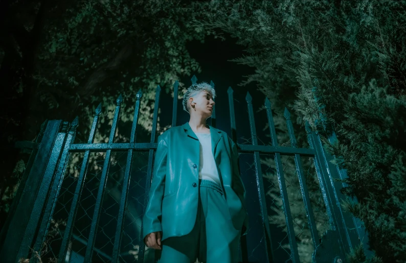 a man in a light blue jacket and dark pants in front of a gate