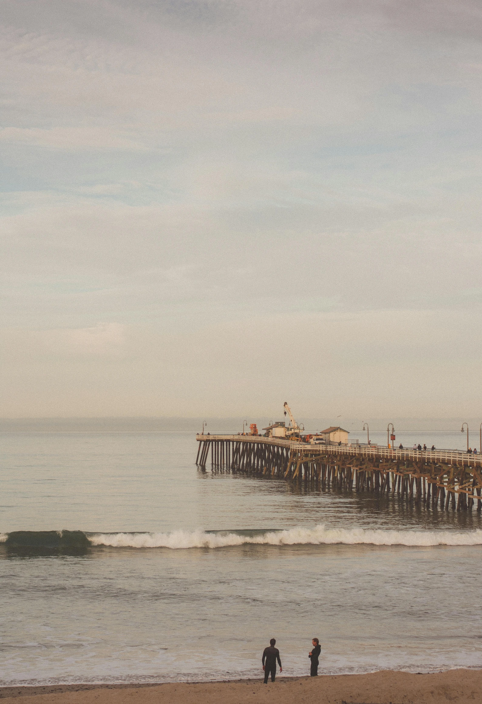 three people walking down the beach towards a pier