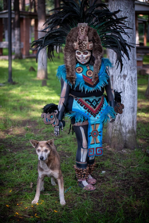 a woman in elaborate dress next to a dog on the grass