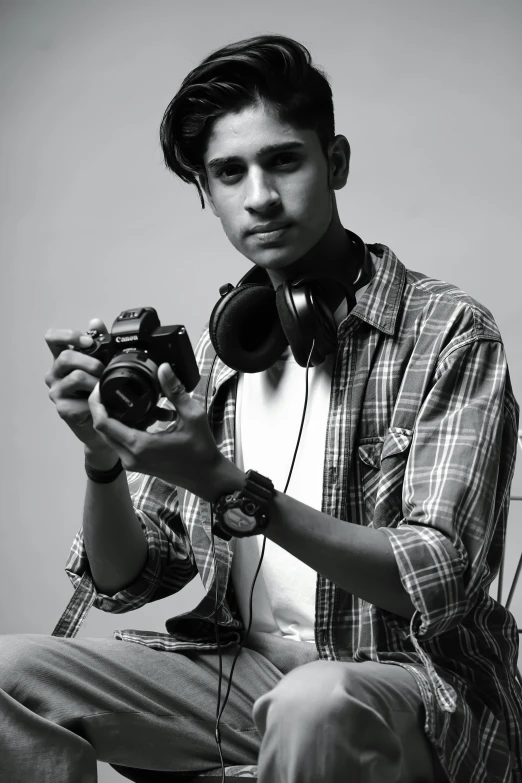 a young man sits holding a camera and two phones