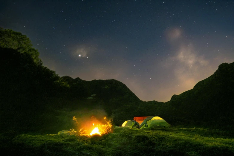 an open tent pitched on top of a green mountain at night