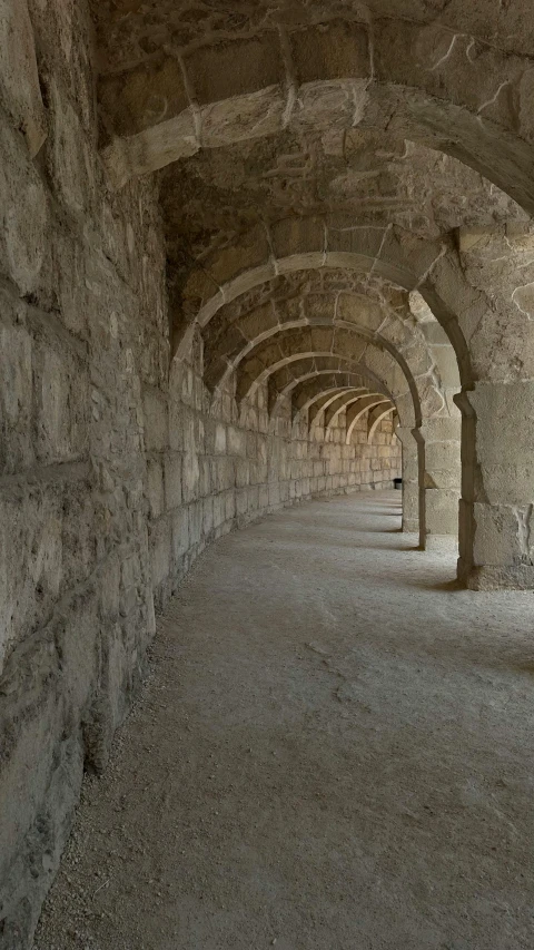 a narrow walkway with archways and benches lined up against the wall