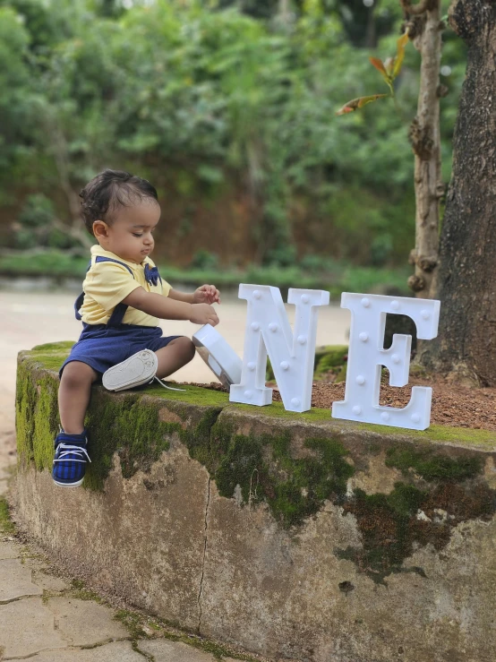 a child sitting on the curb beside a tree holding onto a letter