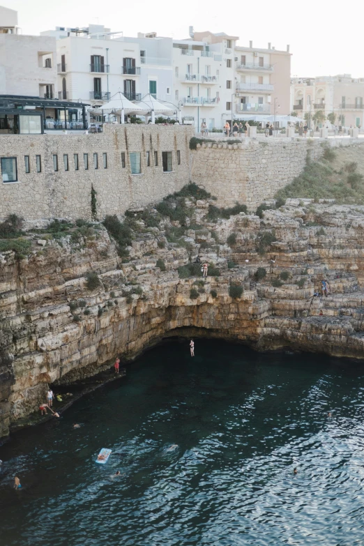 people enjoying their swim in the water by an old brick wall